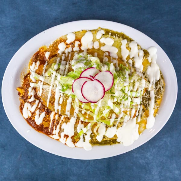 A plate of enchiladas covered in red and green sauce, topped with lettuce, cheese, sour cream, and radishes.