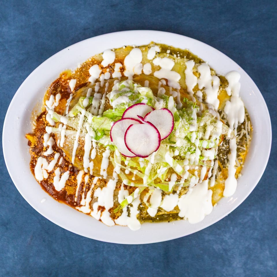 A plate of enchiladas covered in red and green sauce, topped with lettuce, cheese, sour cream, and radishes.