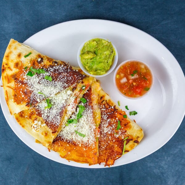 Golden-brown quesadilla slices topped with cotija cheese and cilantro, served with guacamole and salsa.