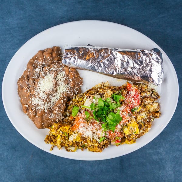 A white plate with refried beans, scrambled eggs with vegetables, and a foil-wrapped burrito.