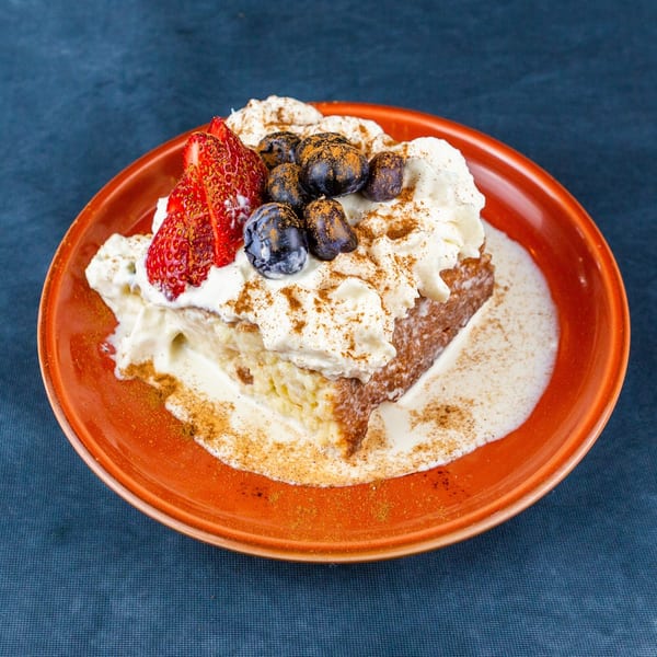 Tres leches cake with whipped cream, strawberries, blueberries, and cinnamon on an orange plate.