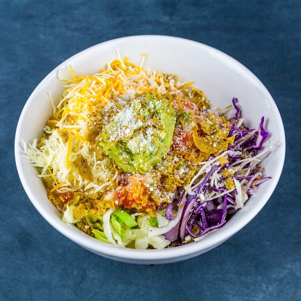 A vibrant salad bowl with shredded cheese, guacamole, lettuce, and purple cabbage.