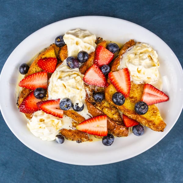 Golden French toast pieces topped with whipped cream, sliced strawberries, and blueberries on a white plate.