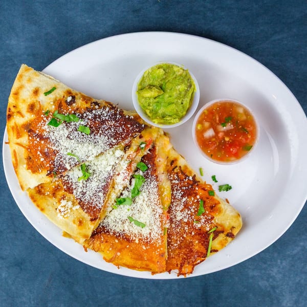 A quesadilla with cheese and cilantro, served with guacamole and salsa on a white plate.