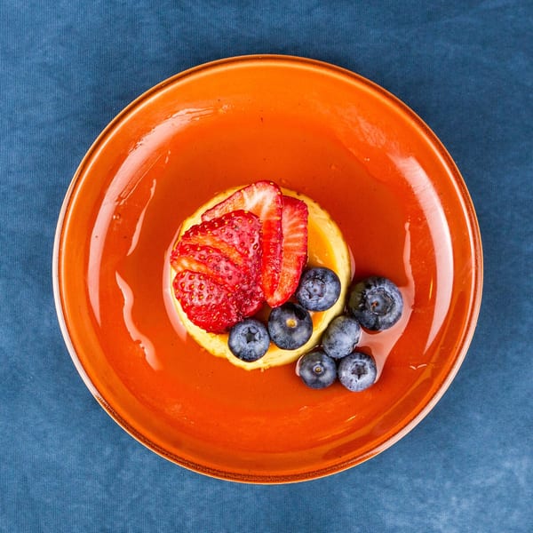 Overhead view of a dessert with strawberries and blueberries on an orange plate.