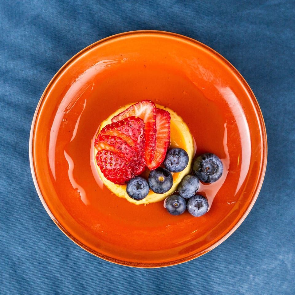 Overhead view of a dessert with strawberries and blueberries on an orange plate.