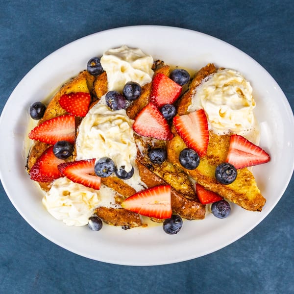 Golden French toast pieces topped with whipped cream, sliced strawberries, and blueberries on a white plate.