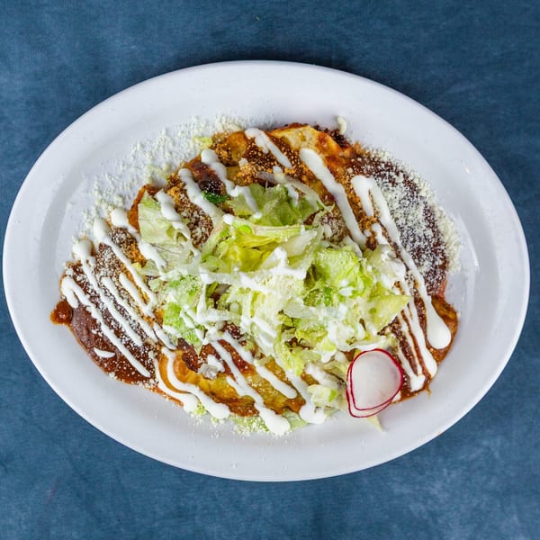 A plate of enchiladas topped with mole sauce, sour cream, lettuce, cheese, and a radish slice.